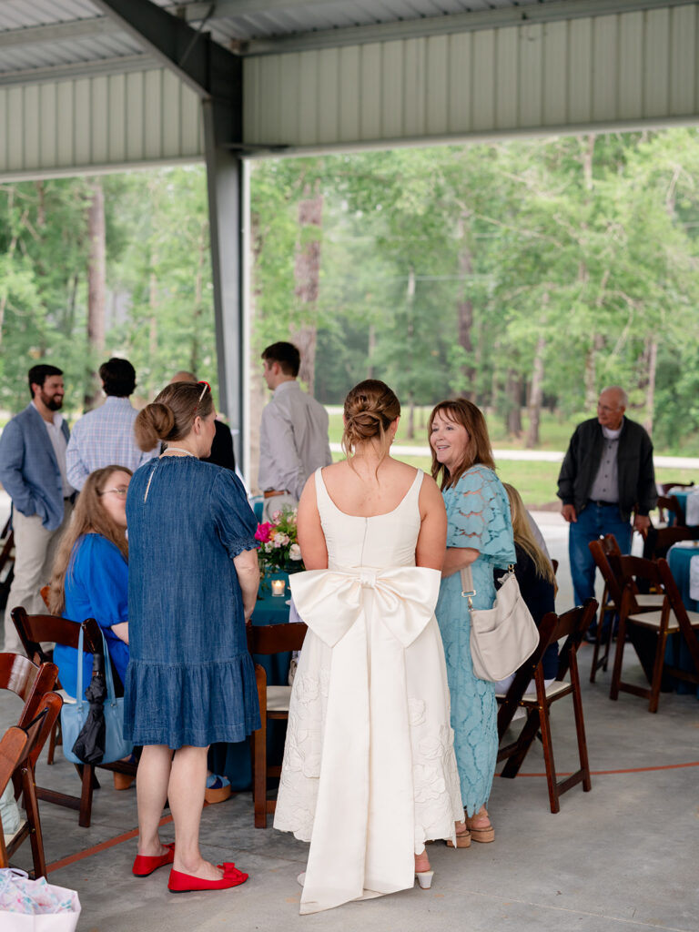 Bride in a white bow dress greeting guests at the rehearsal dinner