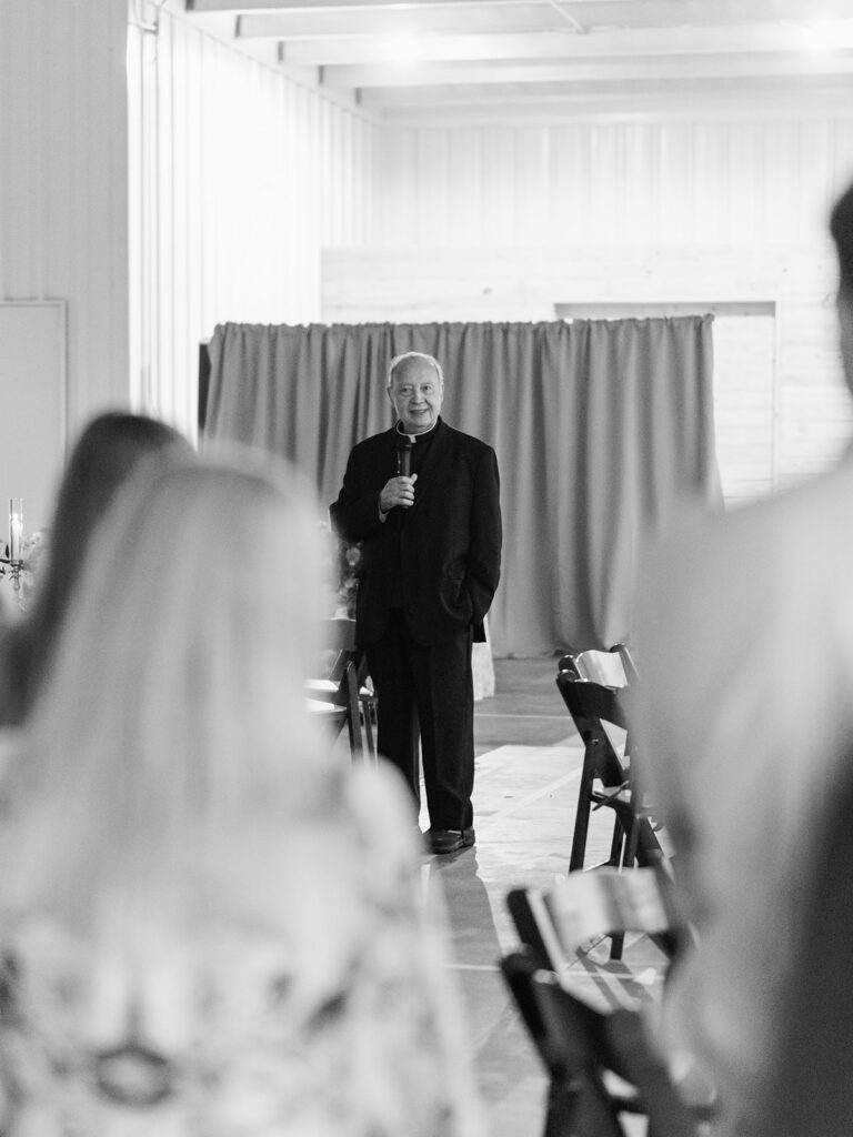 Black and white photo of a priest giving a toast at the rehearsal dinner