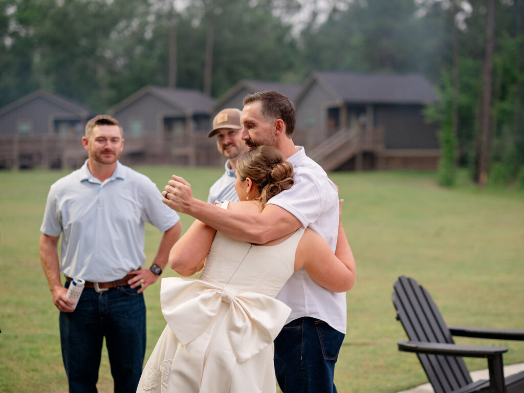 Bride hugging a guest on the lawn in front of the camp cabins