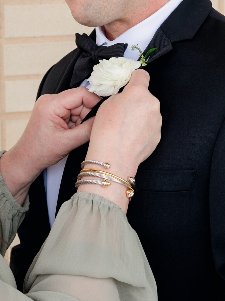 Mother pinning a white rose boutonniere on the groom
