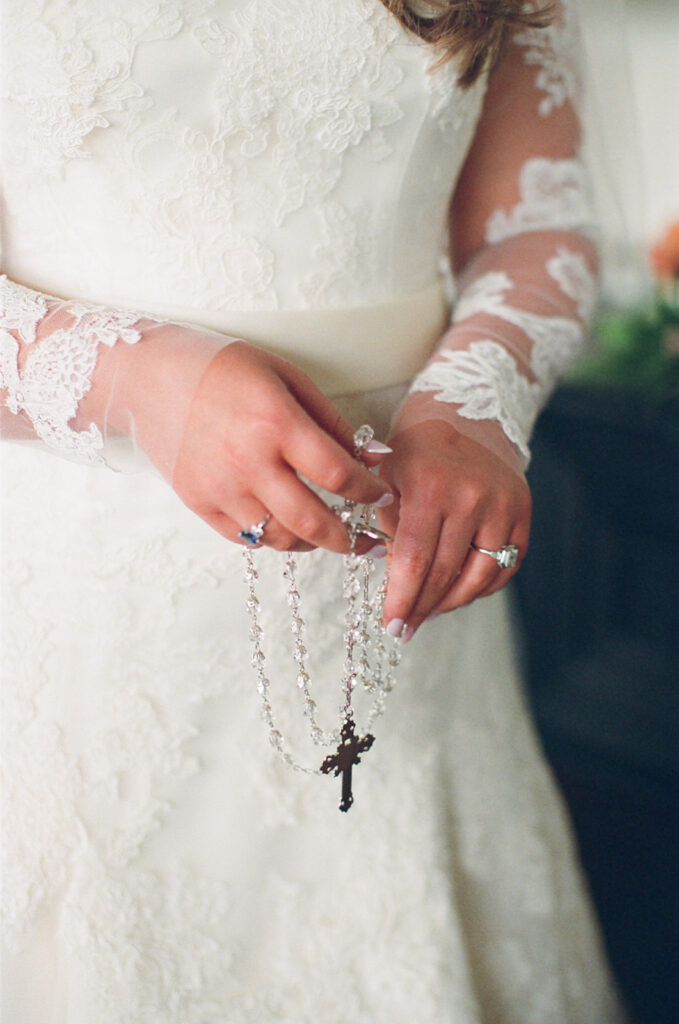 Bride holding a rosary with lace sleeves on her wedding gown, photographed on film