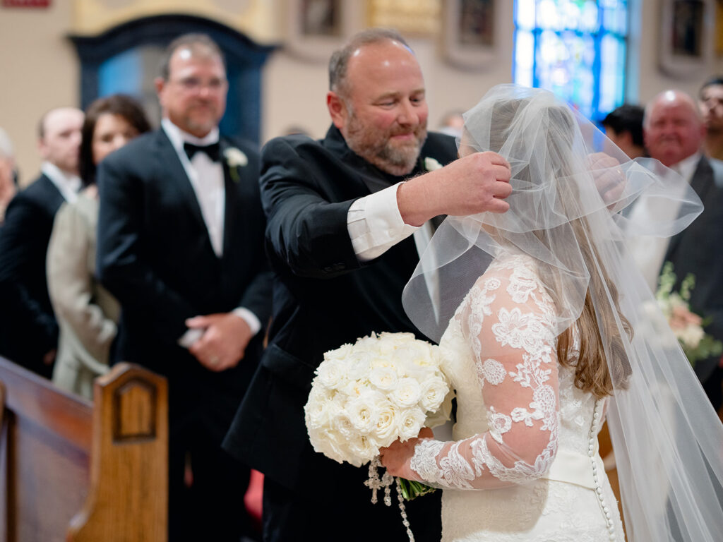 Father of the bride lifting her veil at the front of the church