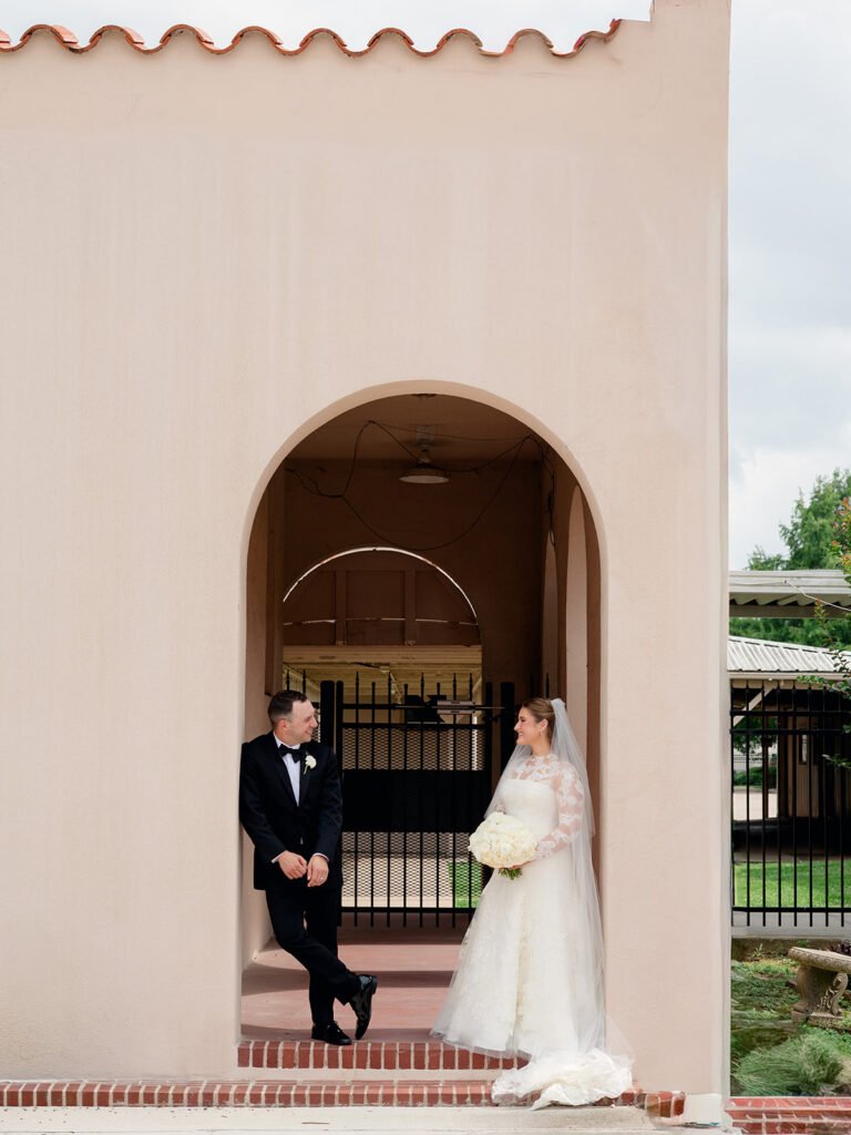 Groom leaning in the church archway while the bride looks on