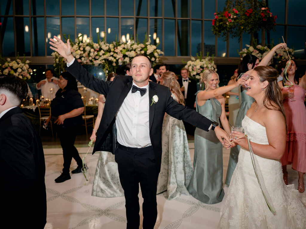 Groom dancing with his arms up surrounded by guests